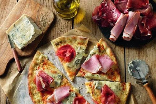 Pizza, jambon, bouteille d'huile d'olive, fromage posé sur une table en bois