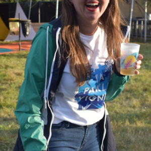 femme souriant dans le champs du festival yapaklévignes, portant le t-shirt et tenant un gobelet